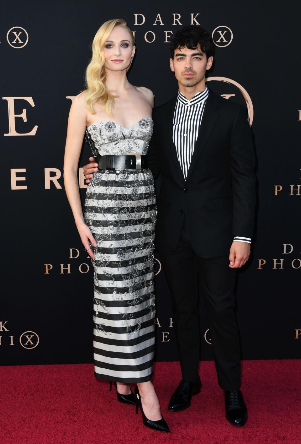 Sophie Turner in a striped dress and heels standing taller than Joe Jonas in a striped shirt and suit.