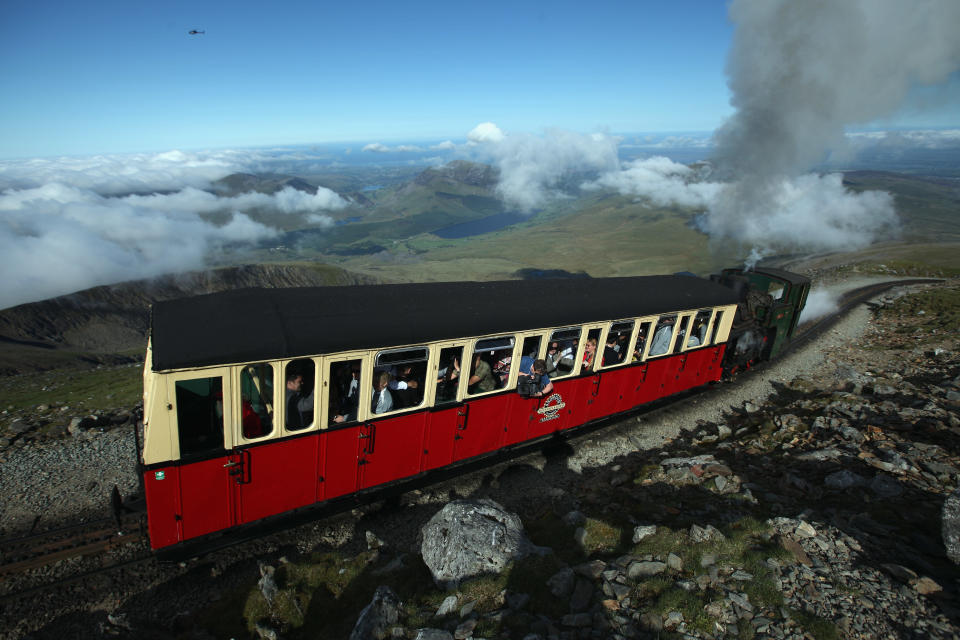 The Snowdon Mountain Railway carries Sir Chris Bonington and the Olympic torch to the summit of Mount Snowdon on May 29, 2012 in Llanberis, United Kingdom. Legendary mountaineer Sir Chris Bonington, aged 77, was given the honour of carrying the torch to the summit of Wales's highest mountain, the place his climbing career began 61 years ago. The Olympic Flame is now on day 11 of a 70-day relay involving 8,000 torchbearers covering 8,000 miles. (Photo by Christopher Furlong/Getty Images)
