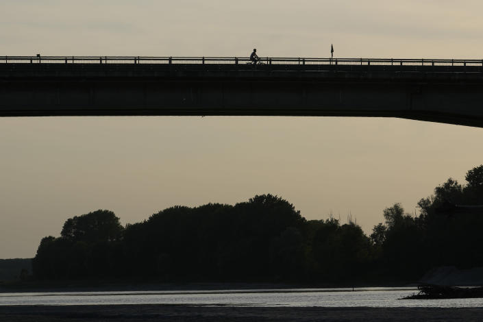 A man bikes on a bridge at sunset, in Boretto, on the bed of the Po river, Italy, Tuesday, June 14, 2022. The drying up of the river is jeopardizing drinking water in Italy's densely populated and highly industrialized districts and threatening irrigation in the most intensively farmed part of the country. (AP Photo/Luca Bruno)