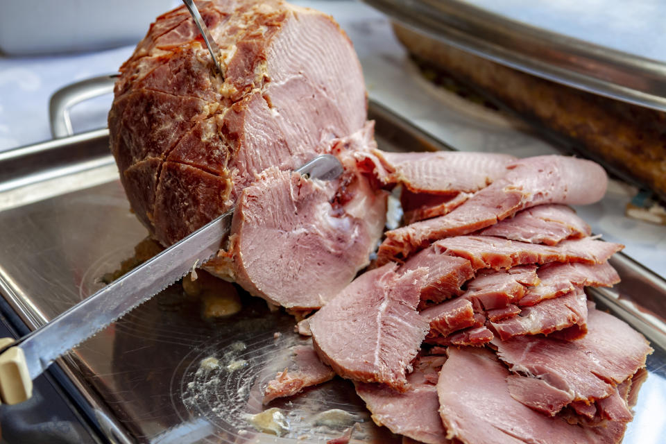 Sliced ham on a platter with a knife, in the middle of being carved