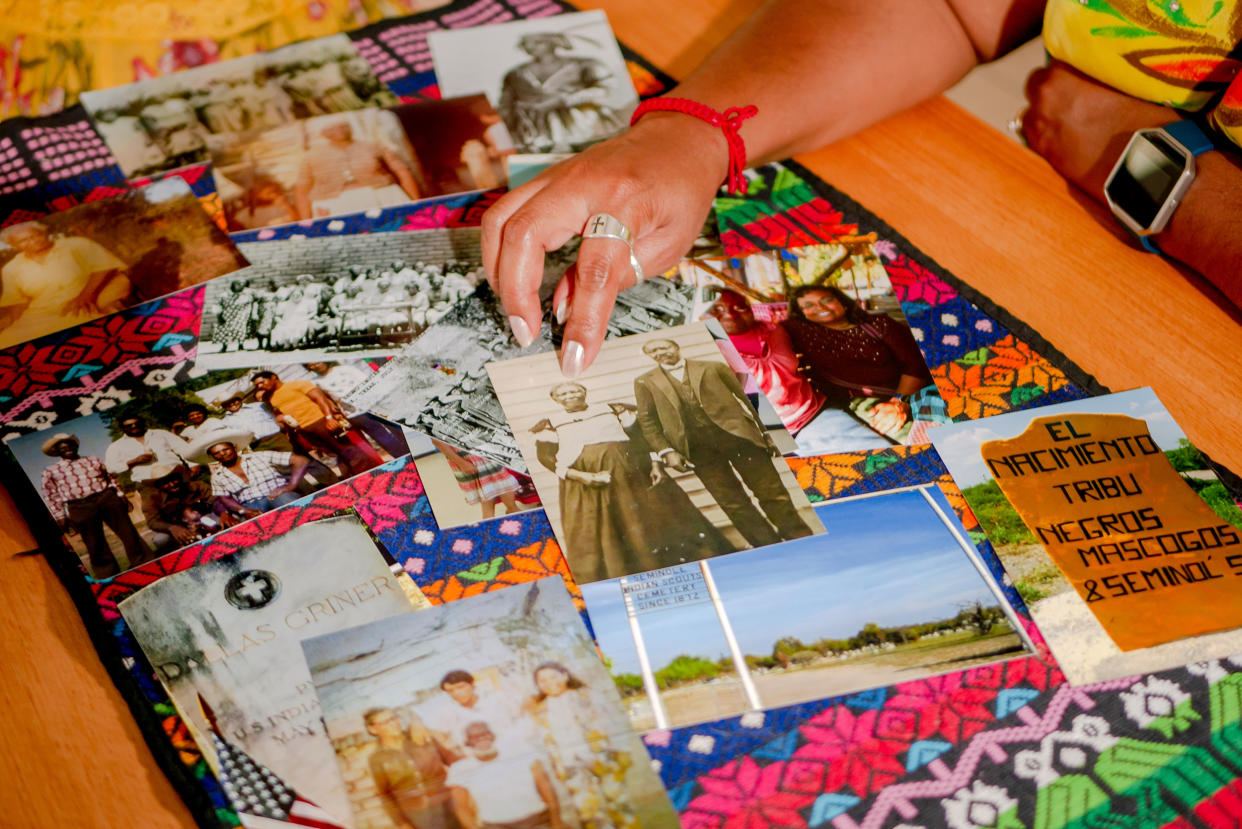 Historical photos displayed on a table including in the center a black and white photo of Corina Torralba Harrington's great grandmother, Effie Payne, whose Mexican name was Felipa Valdes, with her son, Ned Griner, whose Mexican name was Manuel Torralba, in Brackettville, Texas. Bottom right, is a photo of painted rock that marks the direction to Nacimiento de los Negros, Mexico where Juneteenth brings together descendants of Black Seminoles. (Jonathan Israel Castillo / for Telemundo)