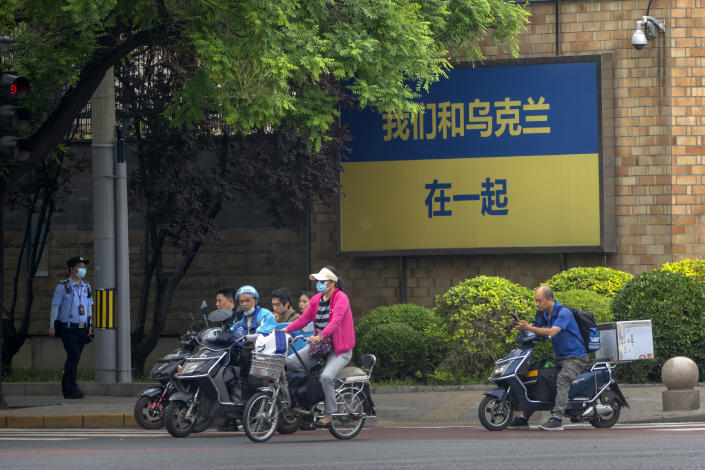 A policeman patrols as people riding bicycles and scooters wait to cross an intersection near a sign reading "We stand with Ukraine" outside the Canadian Embassy in Beijing, Wednesday, May 17, 2023. Embassies in Beijing have been asked by the Chinese government to avoid displaying propaganda after some raised Ukrainian flags or set up placards declaring support for Ukraine. (AP Photo/Mark Schiefelbein)