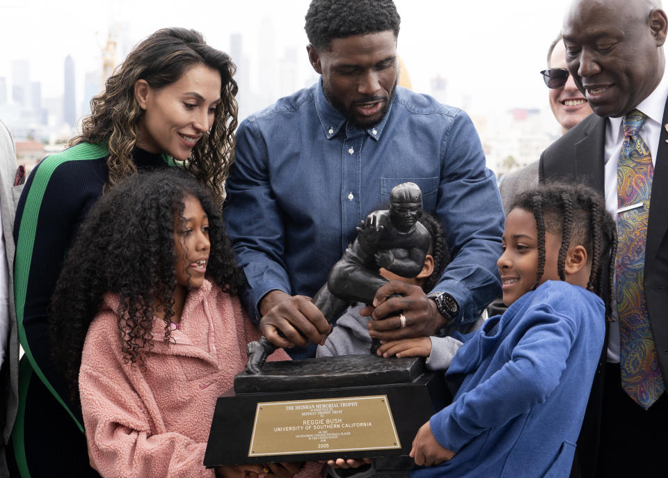 Former USC football player Reggie Bush with his family try to lift a very heavy Heisman trophy for a photo during a news conference at the Los Angeles Memorial Coliseum, Thursday, April, 25, 2024, in Los Angeles. (AP Photo/Richard Vogel)