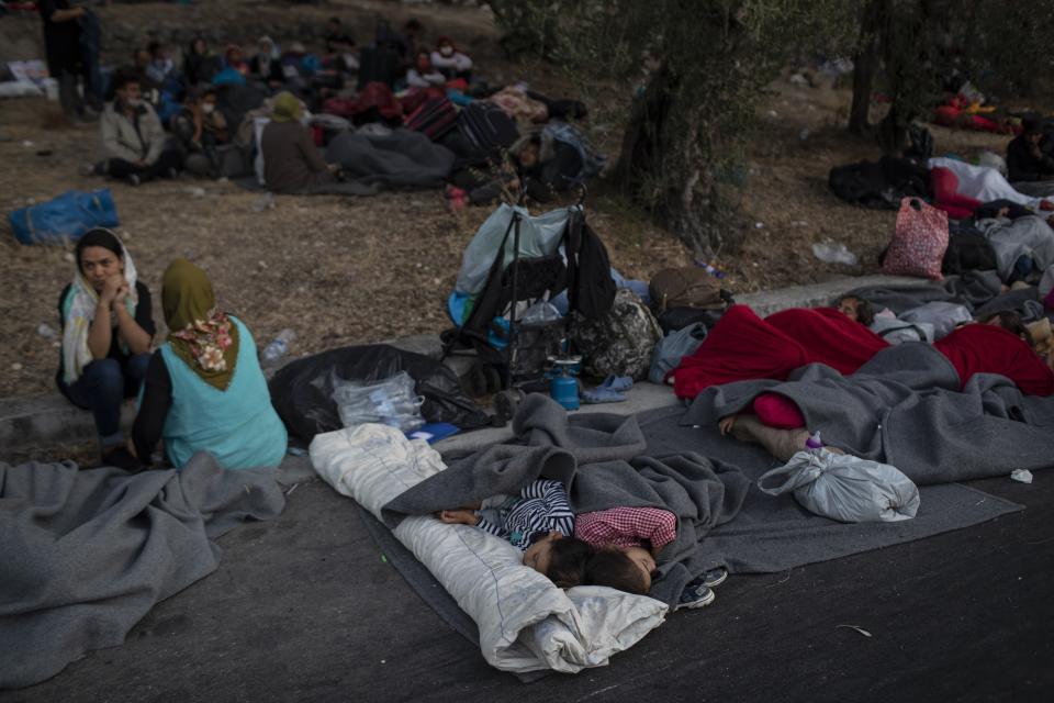 Migrants sleep on the road near the Moria refugee camp on the northeastern island of Lesbos, Greece, Thursday, Sept. 10, 2020. A second fire in Greece's notoriously overcrowded Moria refugee camp destroyed nearly everything that had been spared in the original blaze, Greece's migration ministry said Thursday, leaving thousands more people in need of emergency housing. (AP Photo/Petros Giannakouris)