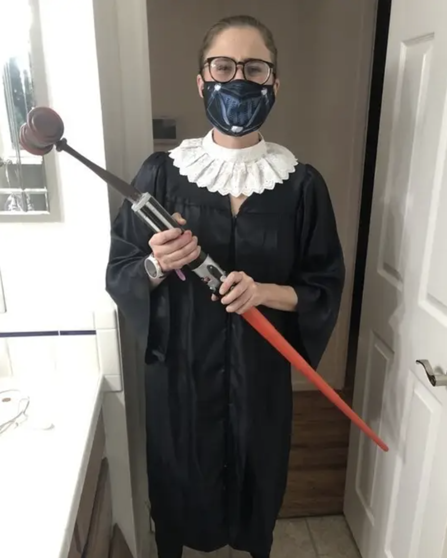 A woman dressed as Ruth Bader Ginsburg...but holding a lightsaber with a gavel on the other end of it