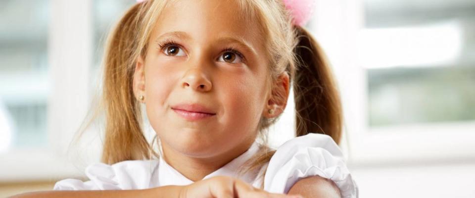 Portrait of a young girl in school at the desk. Horizontal Shot. She is looking and listening at her teacher attentively.