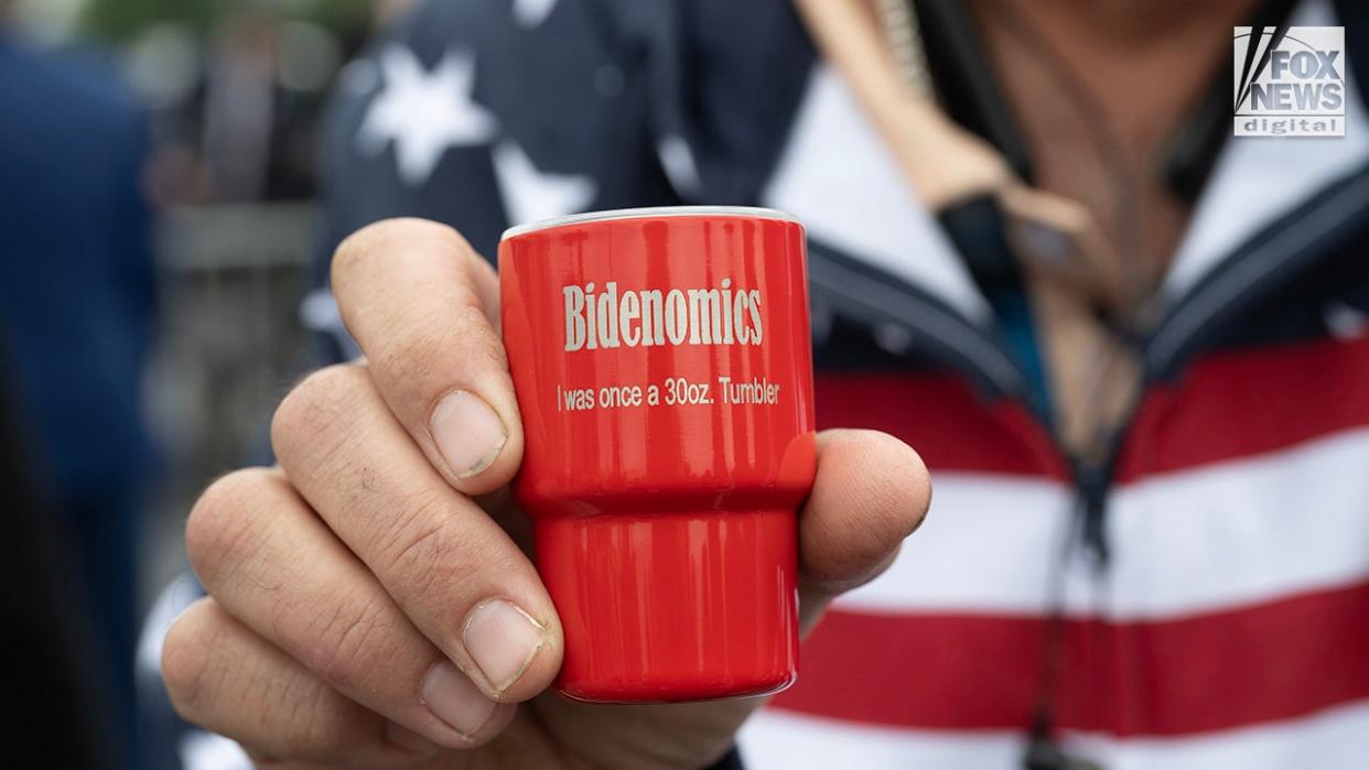 A Trump supporter displays a small tumbler mocking Bidenomics while waiting for former President Donald Trump