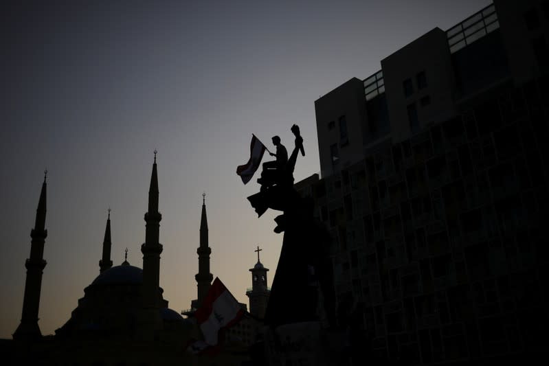 A demonstrator holds a Lebanese national flag as he sits atop a statue on Martyrs' square, as the Al-Amin mosque is seen in the background, during an anti-government protest in downtown Beirut