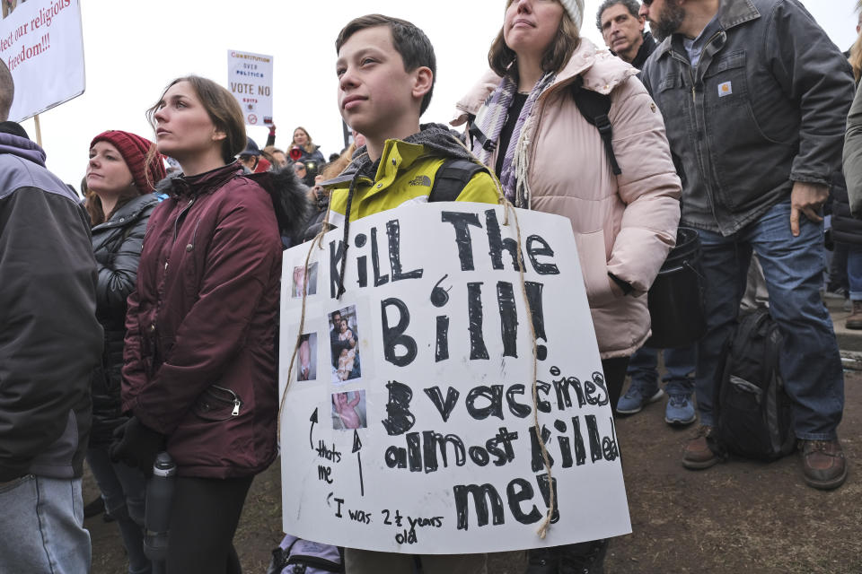 Landon Del Rocco, 11, wears a sign against vaccination during a protest at the state house in Trenton, N.J., Monday, Jan. 13, 2020. New Jersey lawmakers are set to vote Monday on legislation to eliminate most religious exemptions for vaccines for schoolchildren, as opponents crowd the statehouse grounds with flags and banners, including some reading "My Child, My Choice." (AP Photo/Seth Wenig)