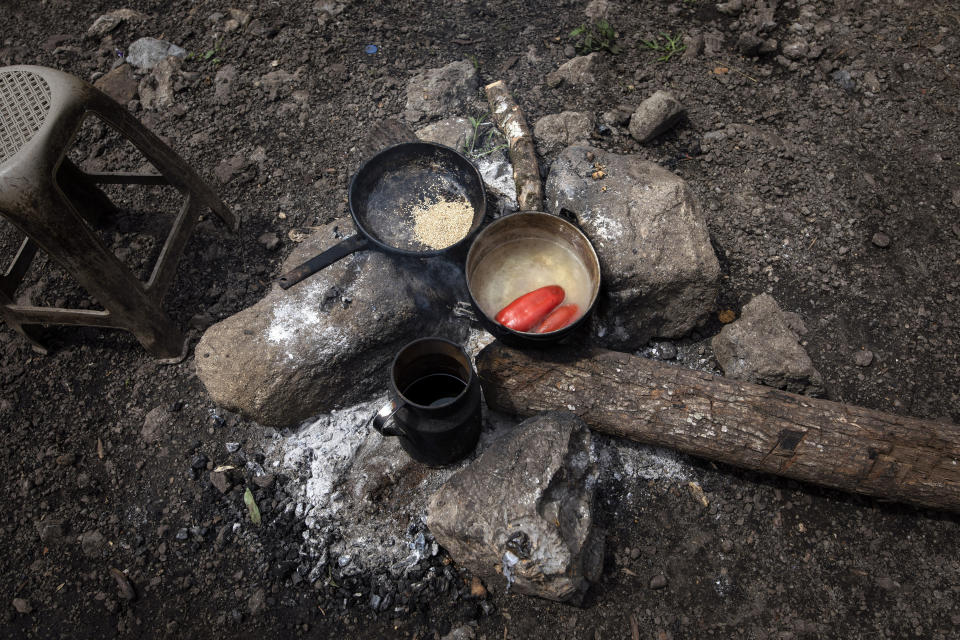 Pots with red chiles and ajonjoli, or sesame seeds, sit on a fire pit, part of a lunch shared in silence by Victor Cal and his parents a day before he left for the United States, in the makeshift settlement Nuevo Queja, Guatemala, Thursday, July 8, 2021. The day before he left for the US was a busy one for Cal. He went from relative to relative, collecting money to buy food during the journey north. (AP Photo/Rodrigo Abd)