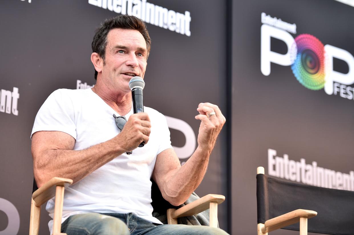 Jeff Probst speaks into a microphone while sitting in a directors chair
