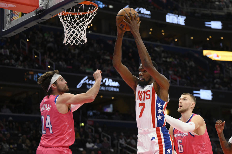 Brooklyn Nets forward Kevin Durant (7) grabs the rebound against Washington Wizards forward Corey Kispert (24) and center Kristaps Porzingis (6) during the first half of an NBA basketball game, Monday, Dec. 12, 2022, in Washington. (AP Photo/Nick Wass)