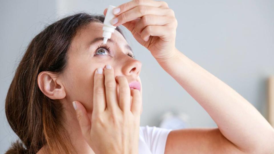 Young woman putting eye drops at home