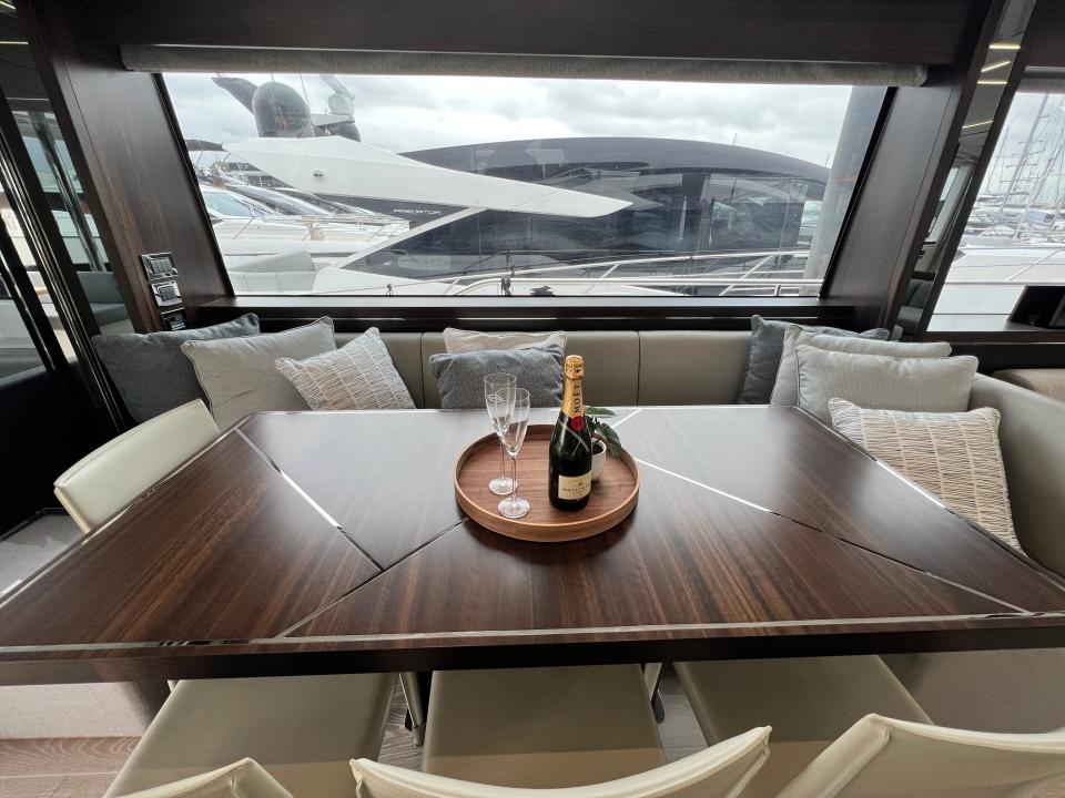 The dining table on a yacht with seating space for eight, a tray with a bottle of champagne on top of the dark wood table with ornate metal adornment