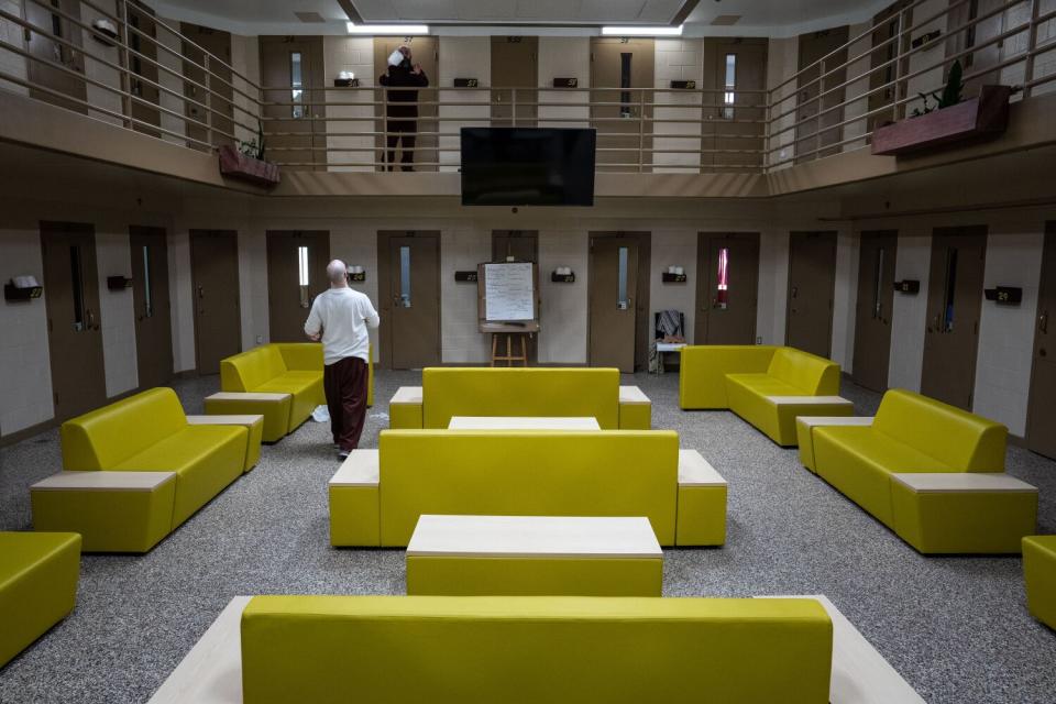 An inmate tosses toilet paper to the second floor, where another inmate stacks the rolls outside cells.