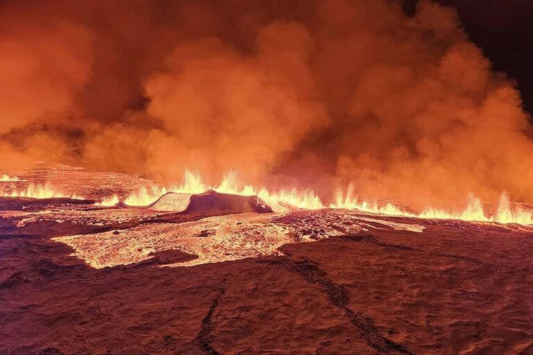 En esta imagen distribuida por el Departamento de Protección Civil y Gestión de Emergencias de Islandia se ve humo y lava fluyendo y tiñendo el cielo de naranja durante una erupción volcánica en la península de Reykjanes, 3 km al norte de Grindavik, al oeste de Islandia, el 19 de diciembre de 2023.