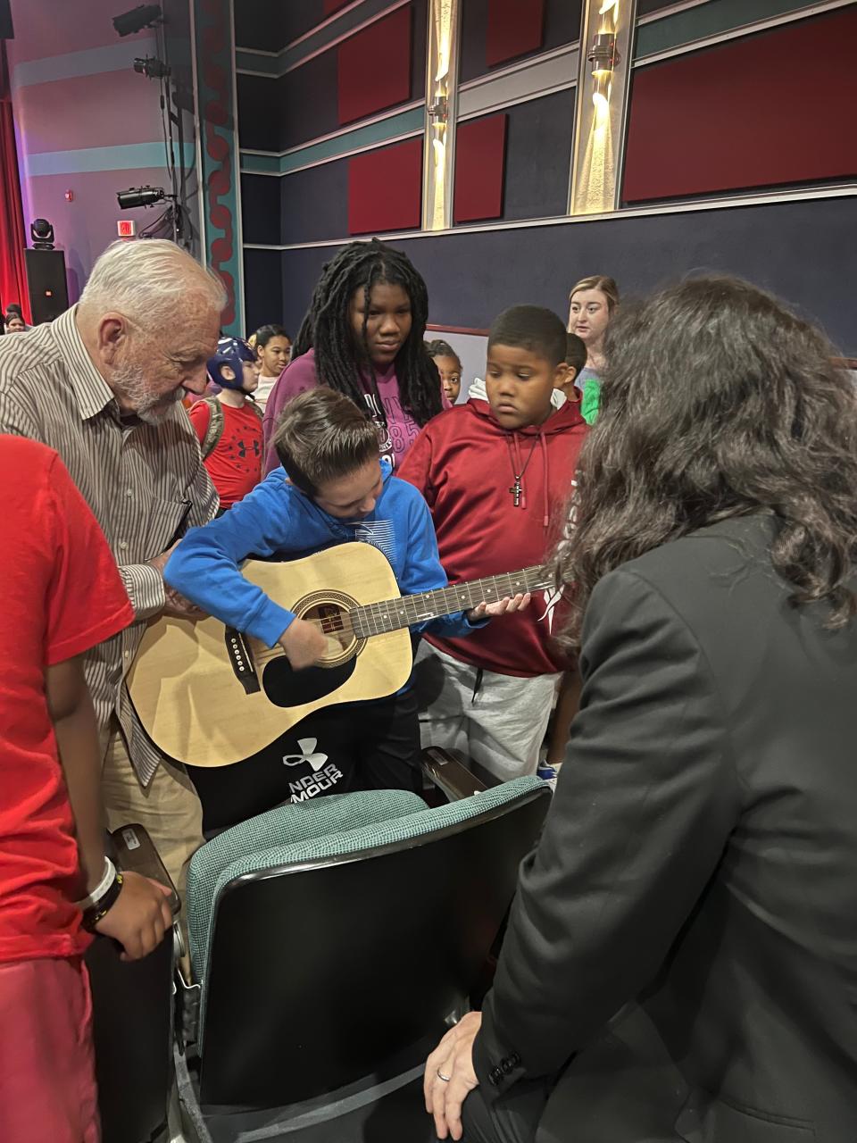 Local musician and volunteer, Sandy Carlton, shows students how to hold and strum a guitar at the Don Gibson Theater Tuesday. Students had the opportunity to learn more about Bluegrass and the counties musical heritage.