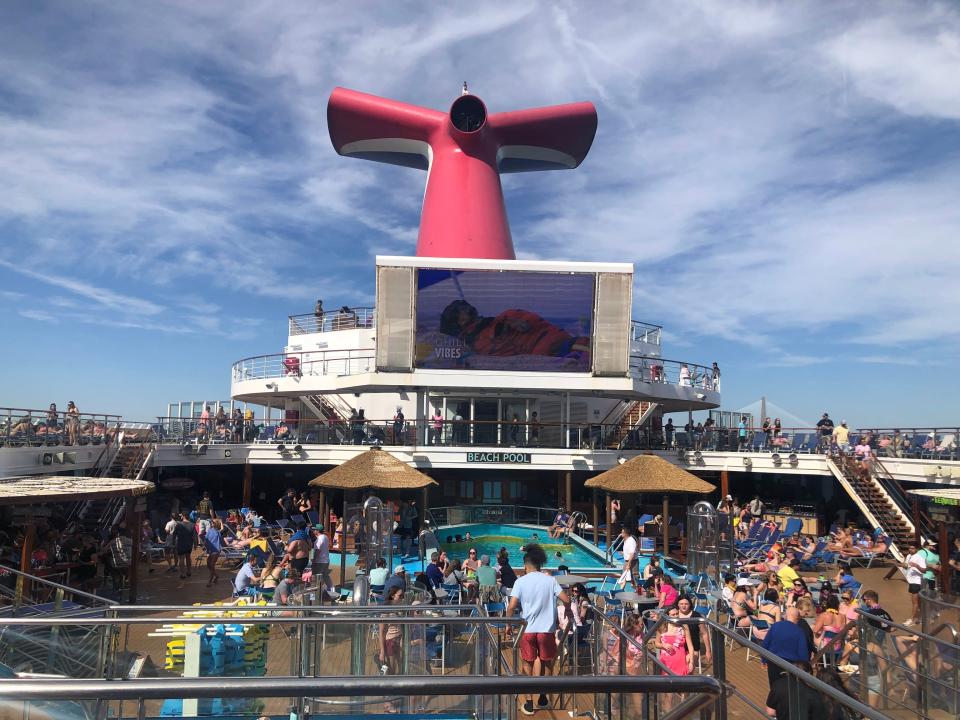 Carnival cruise ship deck filled with people around a pool in front of a large screen