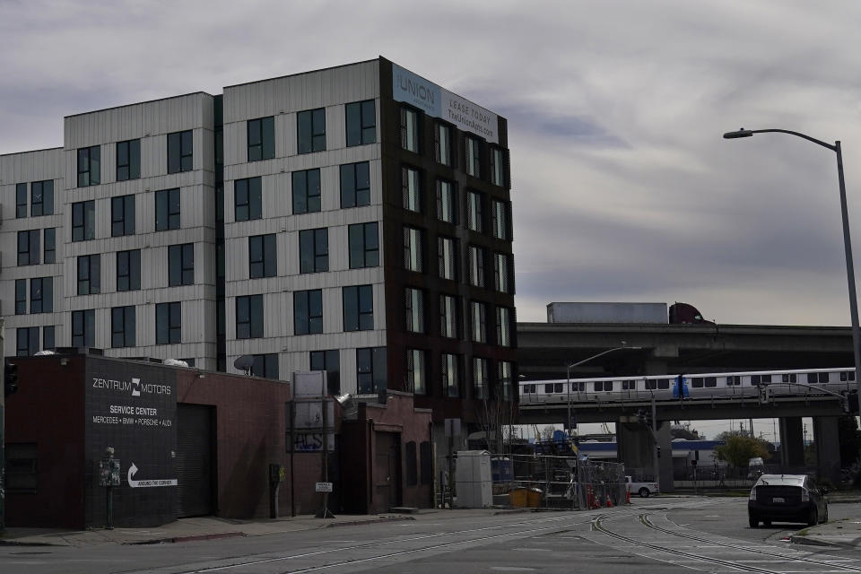 A truck and a BART train drive behind an apartment building in Oakland, Calif., Thursday, Feb. 18, 2021. Disadvantaged communities in America are disproportionately affected by pollution from industry or waste disposal, but their complaints have few outlets and often reach a dead end. (AP Photo/Jeff Chiu)