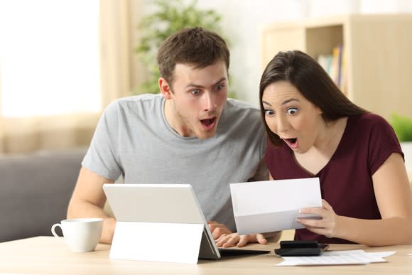 Young couple acting excited over a checkbook and a tablet computer.