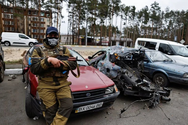 A member of the Ukrainian Territorial Defence Forces sits next to a destroyed car, amid Russia's attack on Ukraine, in Irpin