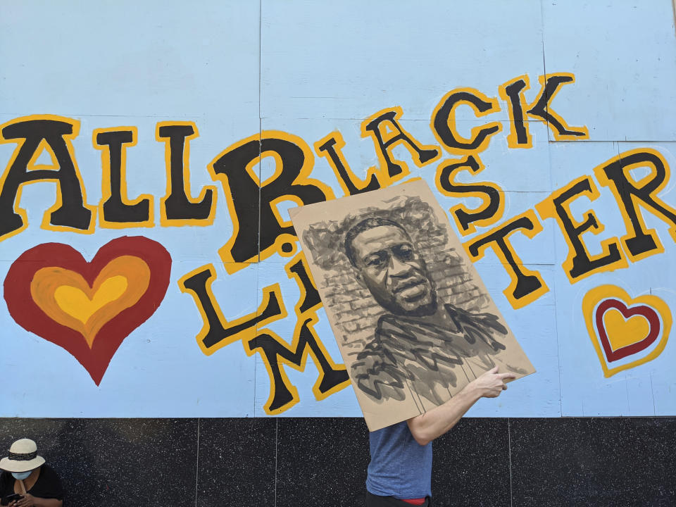 A demonstrator carries an image of George Floyd in front of a boarded up business decorated with a mural reading "All Black Lives Matter," on Hollywood Boulevard, during a march organized by black members of the LGBTQ community in the Hollywood section of Los Angeles. The Black Lives Matter Global Network Foundation, which grew out of the creation of the Black Lives Matter movement, is formally expanding a $3 million financial relief fund that it quietly launched in February 2021, to help people struggling to make ends meet during the ongoing coronavirus pandemic. (AP Photo/Damian Dovarganes, File)