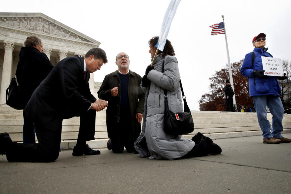 <p>Rev. Brad Wells, left, Rev. Patrick Mahoney, and Paula Oas, kneel in prayer in front of the Supreme Court, as a counter-protester holds a sign that says “What’s Christian About Discrimination,” while the court hears the ‘Masterpiece Cakeshop v. Colorado Civil Rights Commission’ case, Tuesday, Dec. 5, 2017, in Washington. (Photo: Jacquelyn Martin/AP) </p>