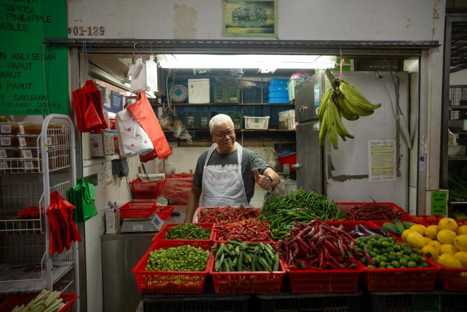A vendor gives the thumbs up behind fresh chiles, beans, okra, eggplant and citrus sold at Geylang Serai market.