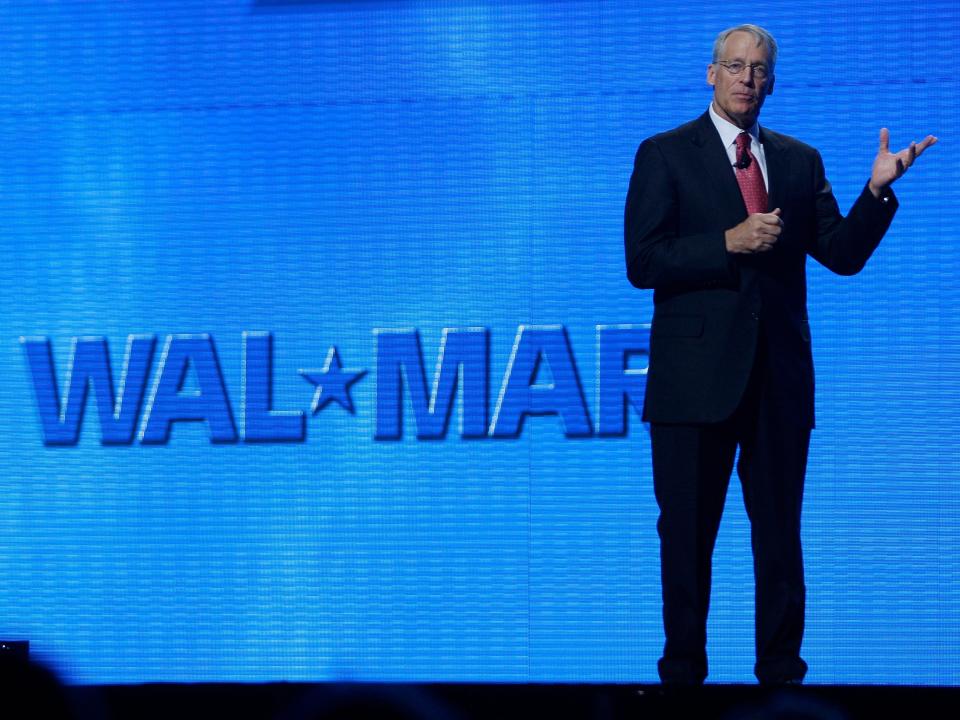 Rob Walton gestures onstage in front of blue Walmart logo