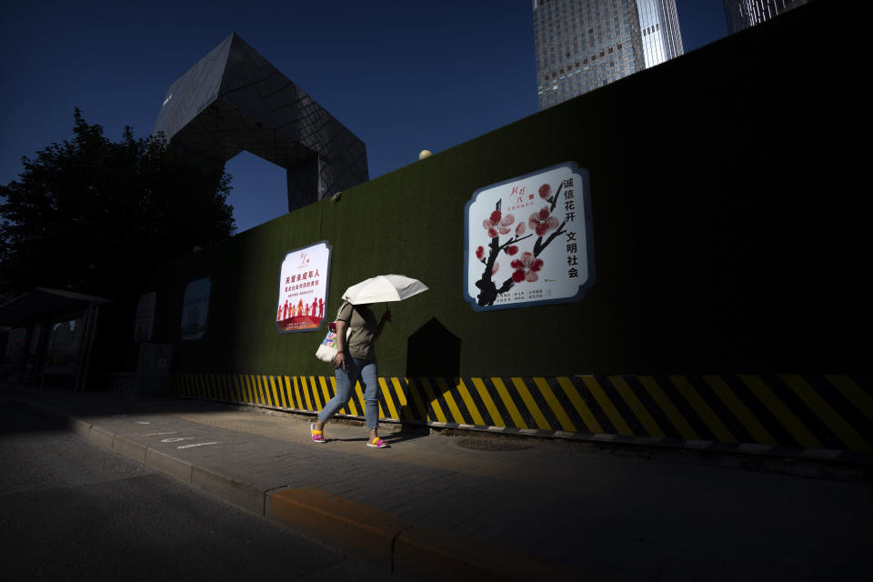 A woman uses an umbrella for shade as she walks through the central business district on an unseasonably warm day in Beijing, Thursday, July 14, 2022. High temperatures have prompted cites in eastern China to open former air raid shelters as a relief from the heat. Temperatures have surpassed all-time records in much of the country, while flooding has hit many parts. (AP Photo/Mark Schiefelbein)