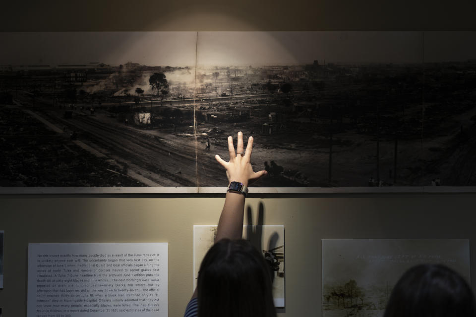 A woman points at a picture of devastation from the Tulsa Race Massacre in a prayer room dedicated to the massacre at the First Baptist Tulsa church during centennial commemorations, Sunday, May 30, 2021, in Tulsa, Okla. The church made the room to provide a place to explore the history of the Tulsa Race Massacre of 1921 and to prayerfully oppose racism. (AP Photo/John Locher)