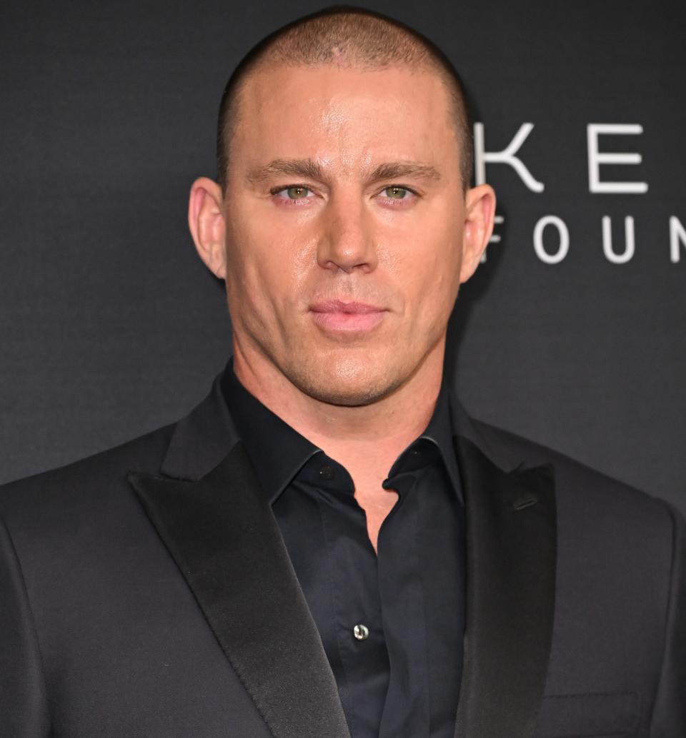 Channing Tatum wearing a dark suit and open collared shirt on a red carpet event