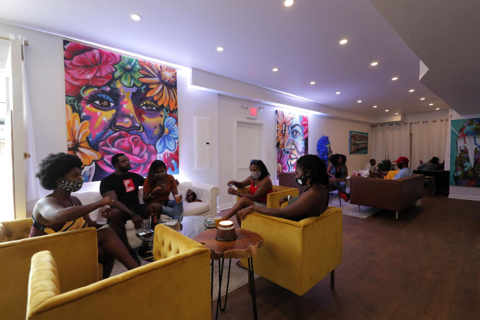 Patrons relax over cocktails in the velvet chairs of DJ Johnson’s NOLA Art Bar in New Orleans on June 23, 2020. In mid-March, the city ordered all bars to close to avoid the spread of the coronavirus. On June 13, Johnson was able to start seating diners inside the gallery at half capacity. He makes constant rounds of the room, distributing hand sanitizer. Gradually, customers are beginning to trickle in. “It’s discouraging. But the only thing that kept me going is, there is no quit,” he said. (AP Photo/Gerald Herbert)