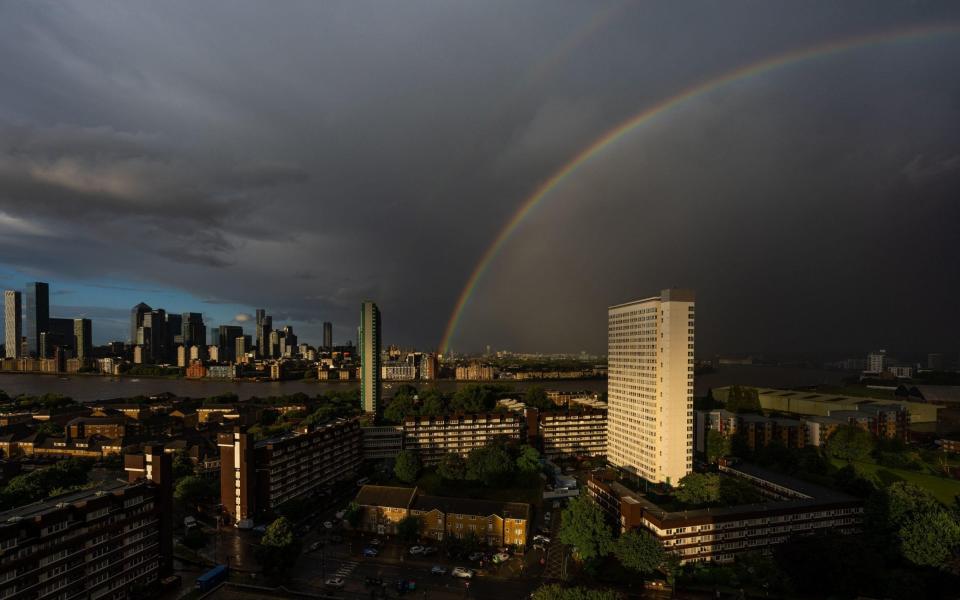 A massive double rainbow begins arcs over east London with Canary Wharf buildings in view (left) as a sunset rainstorm clears - Guy Corbishley/Alamy