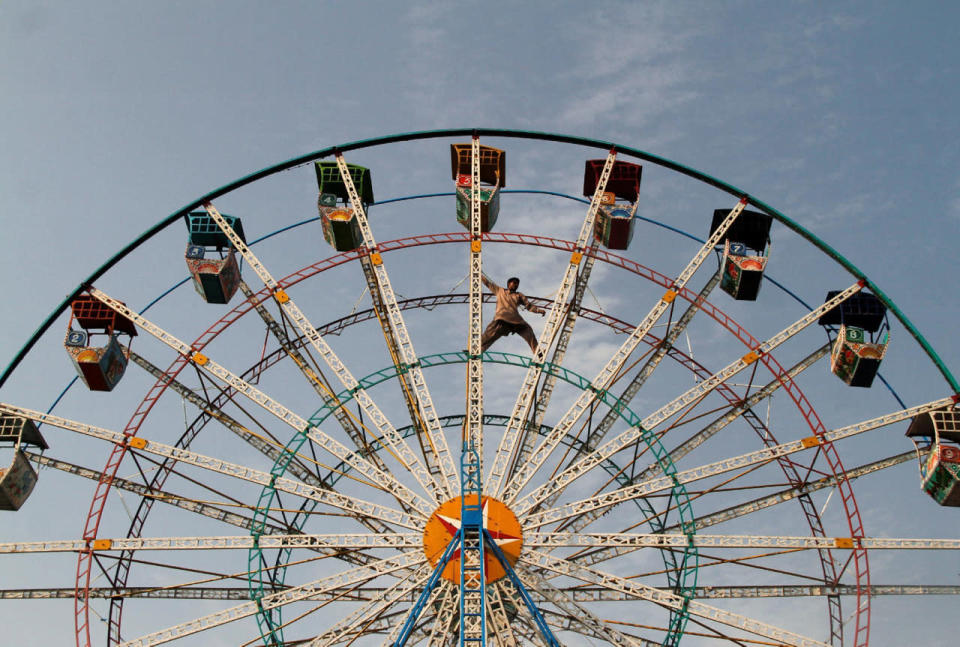 A man balances himself on a Ferris wheel as he inspects it at a public park in Sardaryab, Charsadda