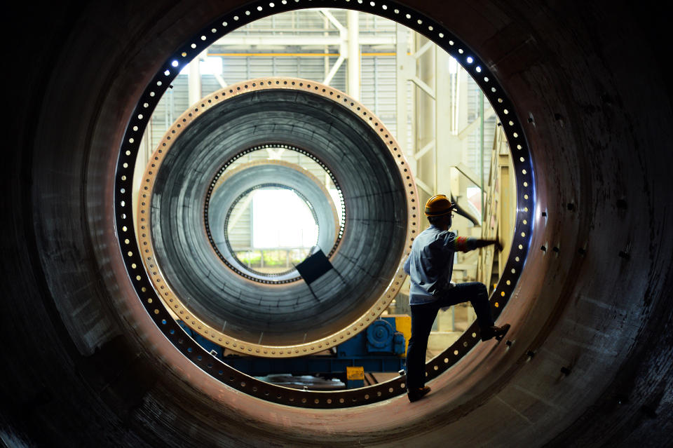 A wind turbine factory worker stands inside a large circular wind turbine component.