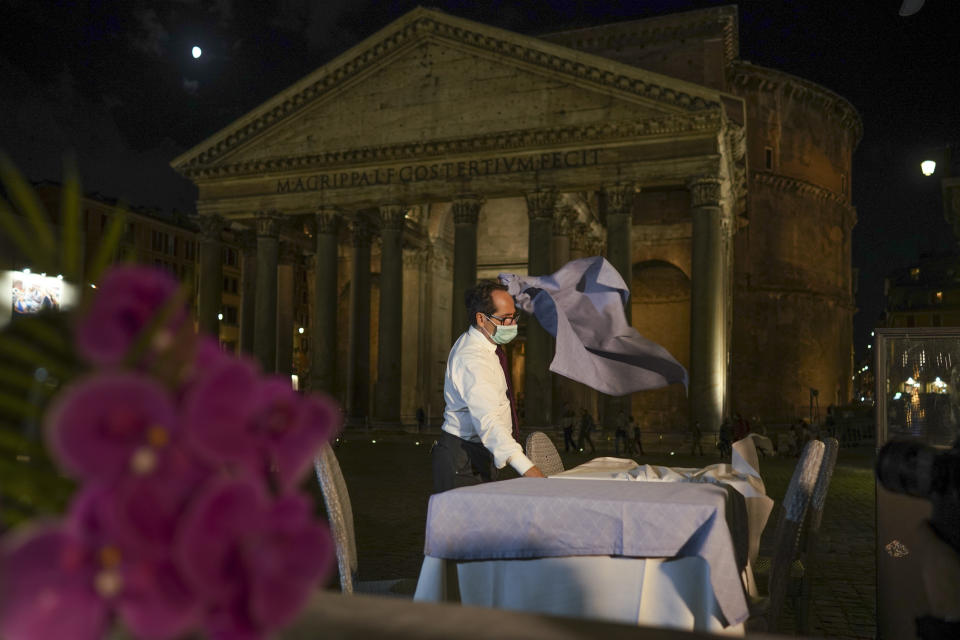 A waiter clears a table before closing a restaurant in front of the Pantheon, Rome, Monday, Oct. 26, 2020. For at least the next month, people outdoors except for small children must now wear masks in all of Italy, gyms, cinemas and movie theaters will be closed, ski slopes are off-limits to all but competitive skiers and cafes and restaurants must shut down in early evenings, under a decree signed on Sunday by Italian Premier Giuseppe Conte, who ruled against another severe lockdown despite a current surge in COVID-19 infections. (AP Photo/Andrew Medichini)