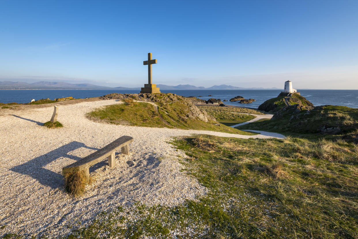 Stone cross and bench on the footpath above Twr Mawr lighthouse. Views across the sea to the mountains of mainland Wales.