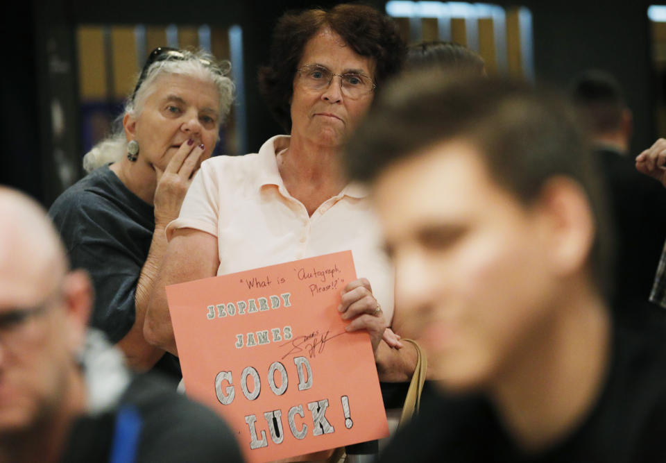 "Jeopardy!" fans Judi Blomquist, holding sign, and Susan Youngblood watch as "Jeopardy!" champion and professional sports gambler James Holzhauer, right, plays in a tournament at the World Series of Poker, Monday, June 24, 2019, in Las Vegas. (AP Photo/John Locher)