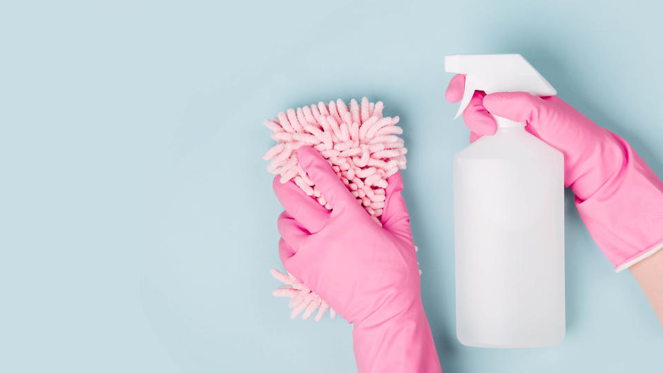 Pink rubber gloves holding a spray bottle and a pink scrubber