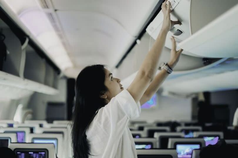 woman passenger in action of trying herself to prepare the bag luggages equips to storage on overhead locker compartment of the airplane, support or h