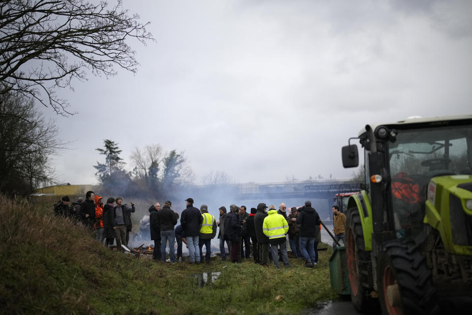 Farmers stand by a bonfire a they block a highway leading to Paris, Friday, Jan. 26, 2024 in Saclay, south of Paris. Snowballing protests by French farmers crept closer to Paris with tractors driving in convoys and blocking roads in many regions of the country to ratchet up pressure for government measures to protect the influential agricultural sector from foreign competition, red tape, rising costs and poverty-levels of pay for the worst-off producers. (AP Photo/Christophe Ena)