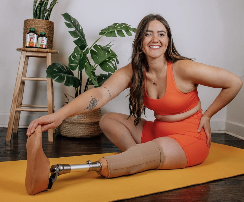 Canadian amputee Allison Lang sits on the ground in an orange two-piece outfit.