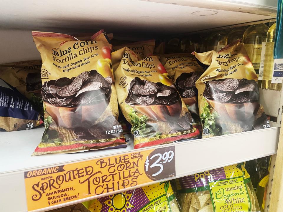 Yellow bags with images of blue-corn tortilla chips sit on gray shelves with an orange sign in front of them at Trader Joe's