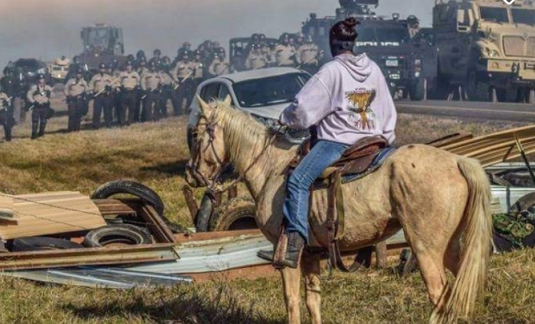<span class="caption">A Native American protester faces police at Standing Rock Reservation in 2016. The campaign against the $3.8bn Dakota access pipeline continues.</span>