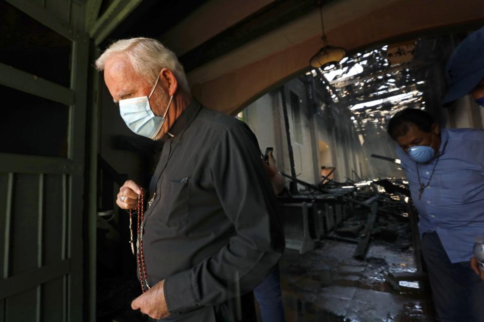 Bishop David O'Connell, wearing a mask, walks out of the doors of the burned San Gabriel Mission