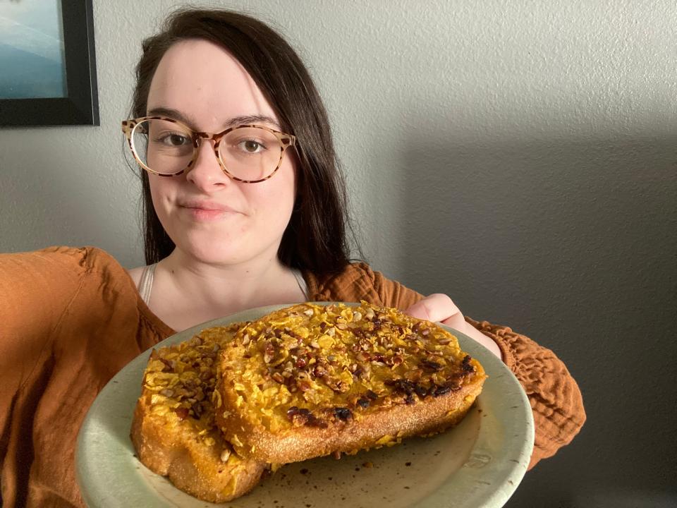 The writer in an orange sweater holding a plate with the pumpkin-pecan-pie French toast