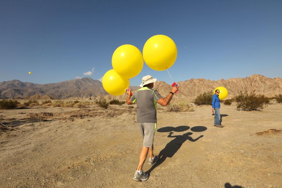 People place yellow balloons in the desert.