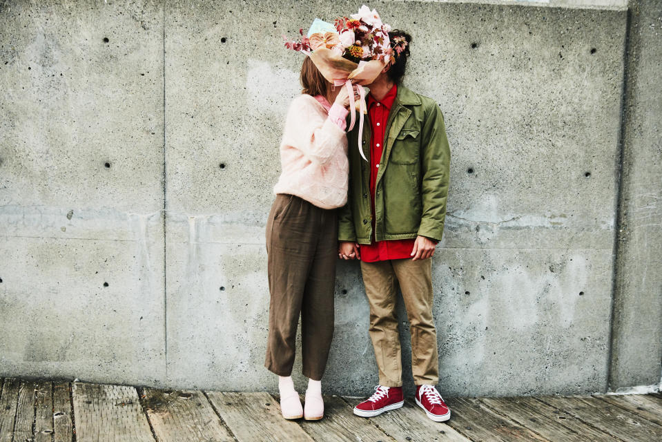 A couple kiss behind a bouquet of flowers.