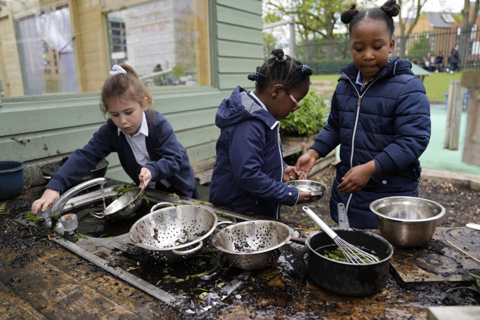 Olivia, left with Elizabeth, and Isla play in the 'dirt' kitchen in the playground of the Holy Family Catholic Primary School in Greenwich, London, Wednesday, May 19, 2021. (AP Photo/Alastair Grant)